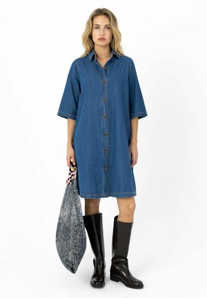Rifľové šaty košeľového strihu s krátkymi rukávmi, s zapínaním na gombíky vpredu a voľným strihom. Doplnkom sú čierne čižmy po kolená a vzorovaná kabelka.