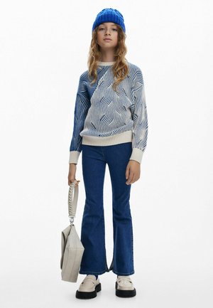 Maglione lavorato a maglia con motivo ondulato blu, base di un leggero crema; jeans a zampa d'elefante in denim scuro; borsa beige con manico intrecciato; scarpe chunky color crema.