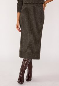 Jupe midi en tricot vert olive à côtes avec des éclats dorés, taille élastique et coupe droite, associée à des bottes bordeaux hautes jusqu'au genou.