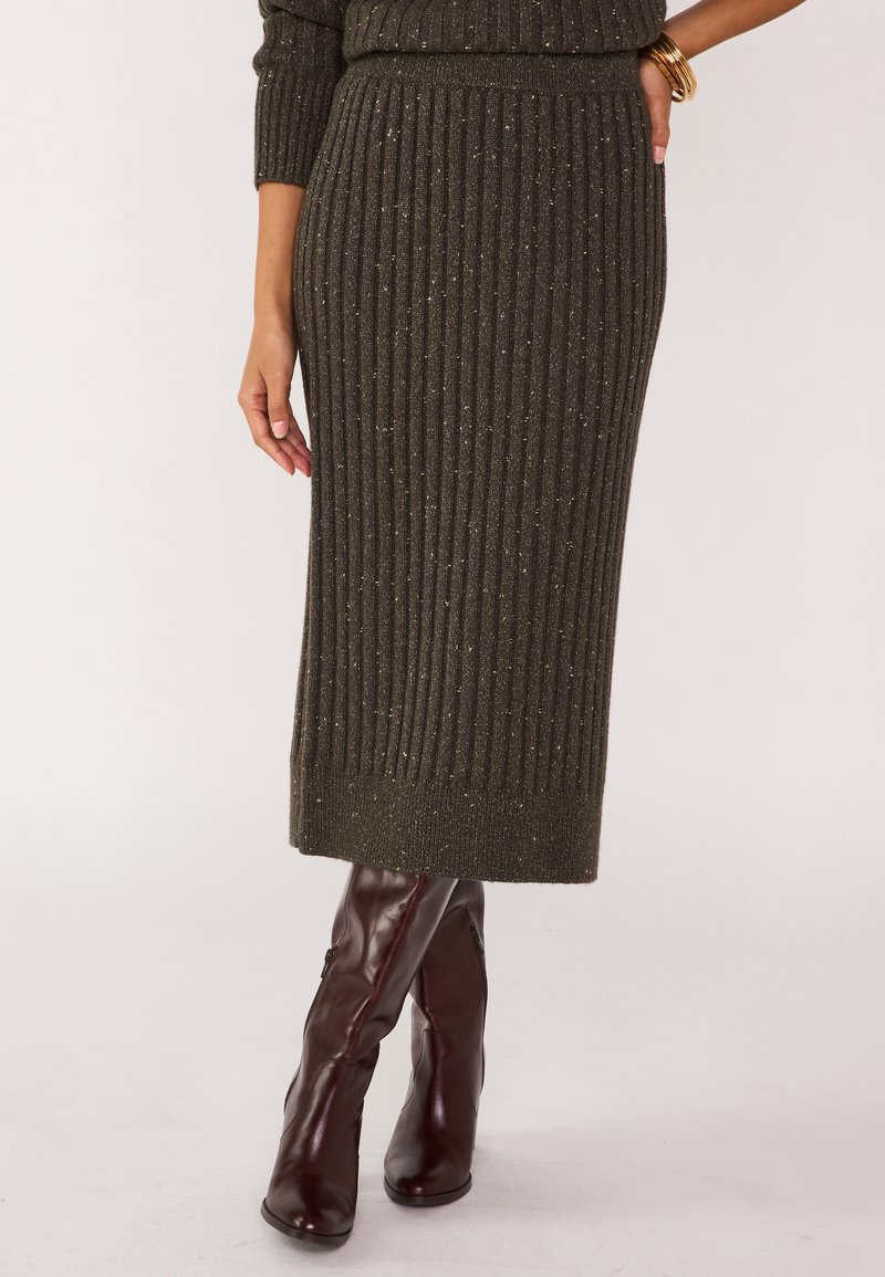 Jupe midi en tricot vert olive à côtes avec des éclats dorés, taille élastique et coupe droite, associée à des bottes bordeaux hautes jusqu'au genou.