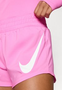 Rózsaszín sportnadrág sima anyagból, elasztikus derékkal és egy nagy, fehér Nike logóval az oldalon.