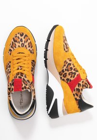 Gula sneakers i mocka med leopardtryck och röda detaljer, svart yttersula och krämfärgad mellansula. Har rund snörning och en vadderad innersula.