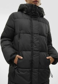 Svart vadderad jacka med huva, med dragkedjefickor på sidorna och ett quiltat mönster. Justerbara snoddar i huvan för passform.