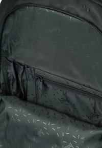 Interno di uno zaino in tessuto nero con più tasche e un comparto con zip, caratterizzato da un sottile motivo con accenti grigio chiaro.