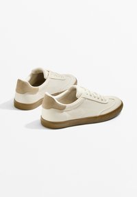 Beige Canvas-Schuhe mit einem Wildlederakzent in Tan an der Ferse, runder Spitze und strukturiertem braunem Gummisohle. Schnürdesign mit dezenten Nähdetails.