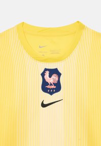 Sárga Nike Dri-FIT mez függőleges fehér csíkokkal, bordázott nyakrésszel, kék emblémával, amelyen rózsaszín kakas és az alatta lévő „FFF” felirat látható.