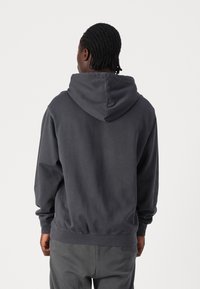 Dunkelgrauer Kapuzenpullover mit lockerer Passform, strukturiertem Stoff und geripptem Saum. Die Rückseite hat ein einfaches Design ohne zusätzliche Grafiken.
