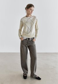 Cream sweater with diamond pattern and black lines, paired with loose grey jeans and black flats. Styled with a white undershirt and belt.