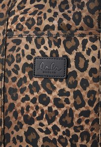 Ύφασμα με λεοπάρ σχέδιο featuring καφέ και μαύρες κηλίδες. Ορατή είναι μια μαύρη ορθογώνια ετικέτα με ανάγλυφο κείμενο "lala BERLIN".