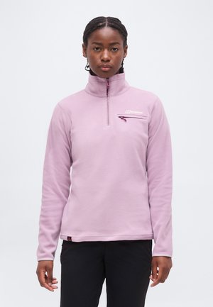 Kobieta w jasnofioletowej bluzie polarowej z suwakiem do ćwiartki i kieszenią na piersi oraz czarnych spodniach, stojąca na jednolitym białym tle.