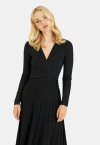 Schwarzes langärmliges Kleid mit V-Ausschnitt, strukturiertem Stoff und plissiertem Rock. Es hat ein eng geschnittenes Oberteil und ein fließendes Saumdesign.