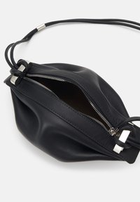 Black leather bag with a soft, rounded shape. Features a zipper closure and silver hardware accents. Adjustable cord shoulder strap.