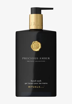 Schwarze rechteckige Flasche mit goldener Pumpe und Deckel. Das Etikett trägt die Aufschrift "Precious Amber" und "Hand Wash" in weißem und goldenem Text. Minimalistisches Design.