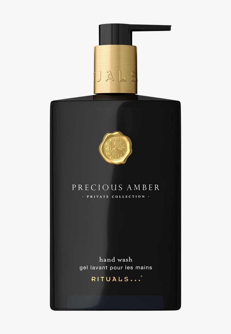 Svart rektangulær flaske med gull pumpe og kork. Etiketten viser "Precious Amber" og "hand wash" i hvit og gull tekst. Minimalistisk design.