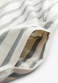 Baumwollstoff mit grauen und weißen wellenförmigen Streifen. Das Bild zeigt einen gefalteten Rand mit einem Taschendetail. Strukturiert Oberfläche mit sichtbaren Nähten.
