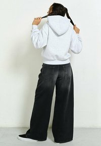 Szara bluza z kapturem i sznurkiem, z dużą kieszenią, w połączeniu z szerokimi czarnymi dżinsami. Gładka faktura, casualowy krój i minimalne detale.