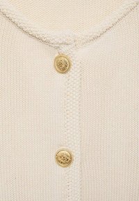 Jasno beżowy sweter kardigan z okrągłym dekoltem, z pojedynczym złotym dekoracyjnym guzikiem oraz wzorem teksturowym na całej powierzchni.