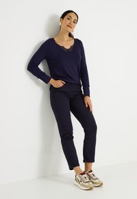 Suéter azul marino de cuello en V con detalles de encaje, combinado con pantalones ajustados azul marino oscuro y zapatillas multicolores con acentos en beige, rojo y marrón.