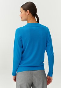 Kobaltblauwe pullovertrui met een geribbelde ronde hals en manchetten. Heeft een relaxed fit en een zachte textuur, gecombineerd met grijze broek.