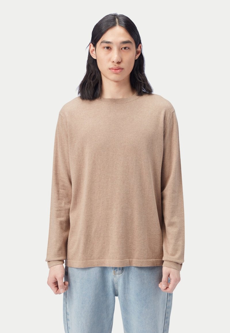 Beiges langärmliges Shirt mit rundem Ausschnitt, aus weichem Stoff. Verfügt über eine lockere Passform und einfache Saumdetails. Kombiniert mit hellblauen Jeans.