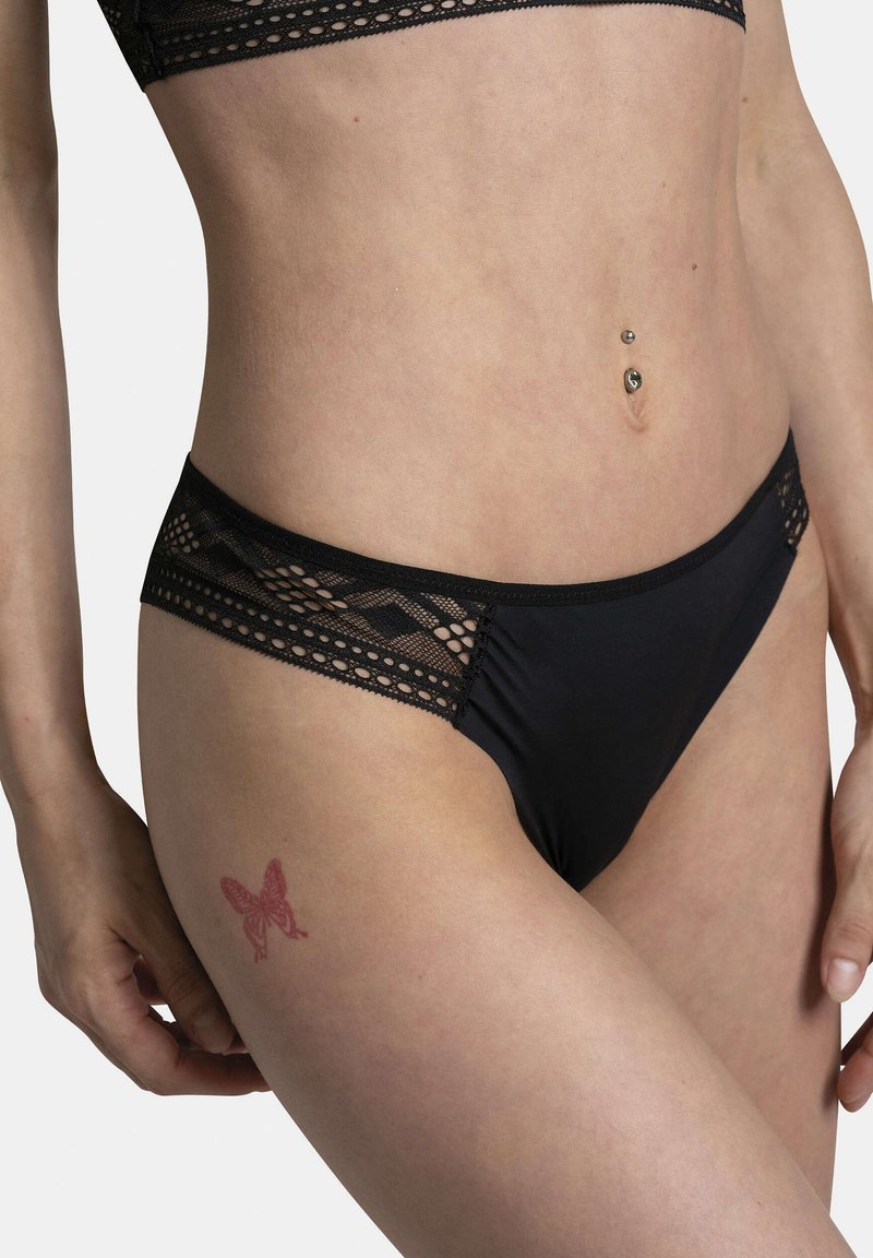 Sous-vêtements noirs à bordures en dentelle, avec un tissu corporel lisse, des motifs géométriques sur la ceinture, et un tatouage de papillon sur la cuisse.