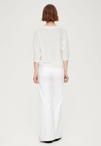 Pull en tricot blanc texturé à manches courtes, avec un large col et un motif côtelé vertical. Assorti à un jean évasé blanc.