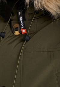 Parka verde oliva con borde de piel sintética; cuenta con herrajes negros y cordones ajustables. Incluye la etiqueta con el logotipo distintivo "SuperDry".
