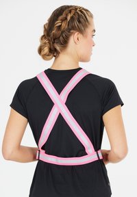 Vaaleanpunainen heijastava valjaat, joissa on ristikkäiset hihnat ja solki, käytetään mustan lyhythihaisen paidan päällä, esittelee toiminnallista muotoilua.