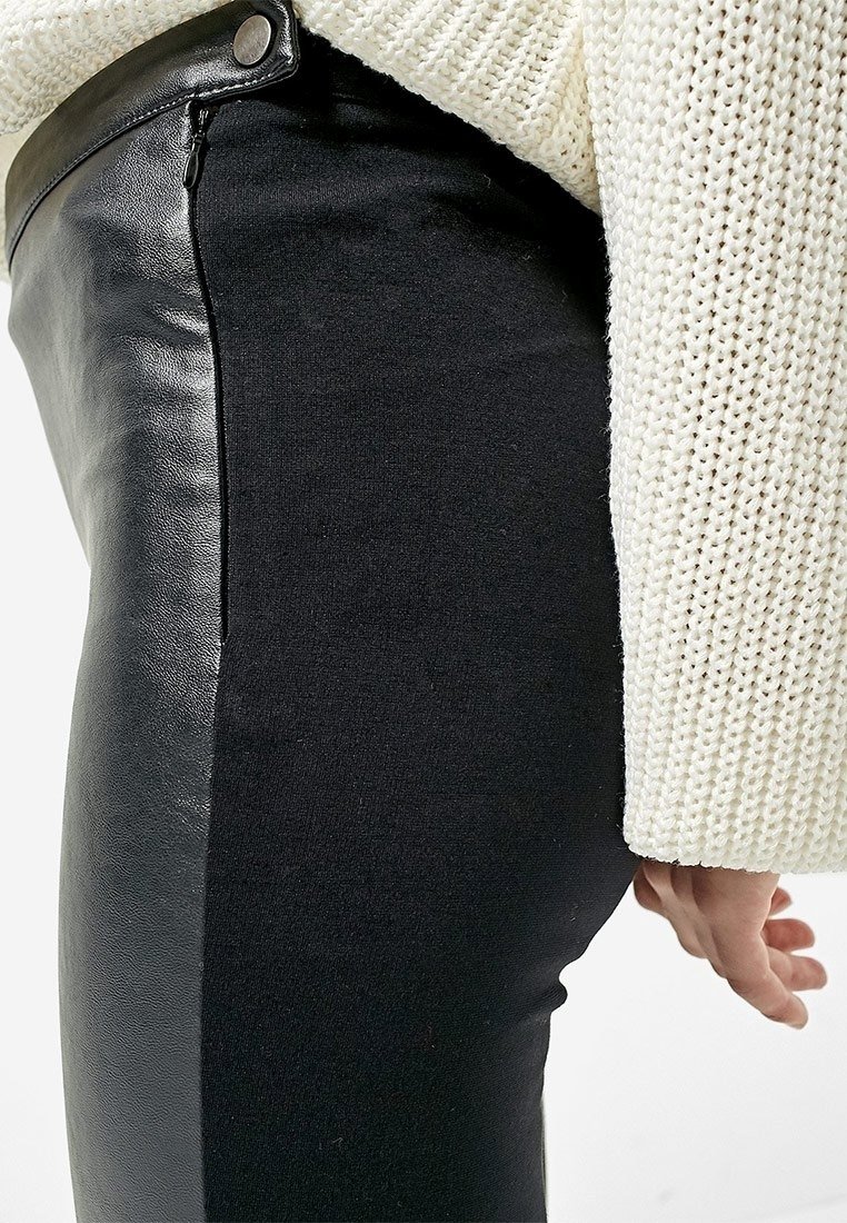 Pantaloni neri con pannelli in pelle sul lato esterno, abbinati a un maglione di maglia crema che presenta un motivo testurizzato.