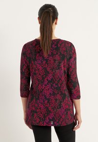 Zwarte top met een bloemenpatroon in rode en paarse tinten, driekwart mouwen, zachte stof en een licht uitlopende taille.