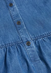 Tissu en denim avec couture froncée sous une patte boutonnée comportant trois boutons métalliques foncés alignés verticalement.