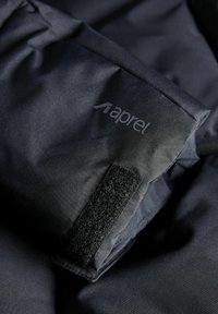 Sort stofjakkeærme med "aprel" logoet, udstyret med velcro-rem og glat tekstur, vist i nærbillede.