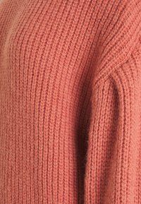 Rippstrickpullover in zartem Korallton. Mit lockerer Passform und strukturiertem Stoff mit sichtbaren Nähten. Gemütliches und warmes Aussehen.