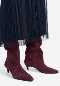 Bordeaux suède enkellaarsjes met puntige neuzen en lage kittenheels, gedeeltelijk bedekt door een geplooide hoogblauwe tule rok.