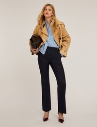 Beige trenchcoat, lysblå skjorte med knapper, mørke skræddersyede bukser og burgunder højhælede sko, med en sort håndtaske holdt under den ene arm.