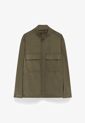 Olivgrön, mockaliknande tygjacka med ståkrage, tryckknappar och två bröstfickor. Har en rak skärning och minimala sömmar.