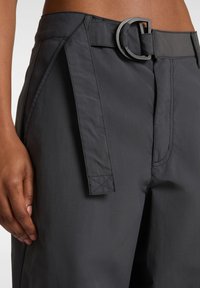 Pantaloni grigi leggeri con vita con cintura, fronte piatto e dettagli di cucitura laterale. Texture liscia con design raffinato e minimalista.