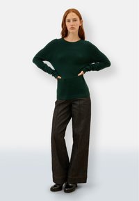 Grüner Strickpullover mit langen Ärmeln und Rundhalsausschnitt, kombiniert mit weit geschnittenen, dunklen Jeans mit Kontrastnähten und schwarzen Plateauschuhen.