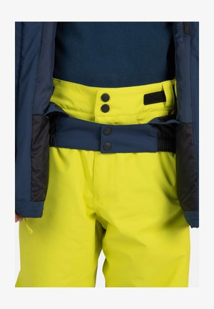 Helle gelbe Skihosen mit einem kontrastierenden marineblauen Bund, ausgestattet mit zwei schwarzen Druckknöpfen und Elastik für eine verstellbare Passform.