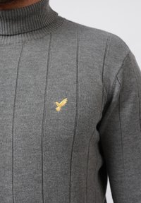 Grau gerippter Rollkragenpullover aus Strickstoff. Verfügt über vertikale Streifen und ein kleines goldenes Vogel-Logo auf der Brust. Klassische Passform.