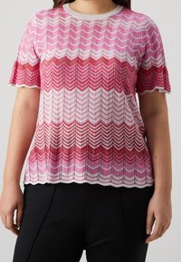 Svetr s krátkým rukávem pletený v růžovo-červeném chevron vzoru, se strukturovanými vlákny a vlnitým lemem, doplněný bílým obrysem.