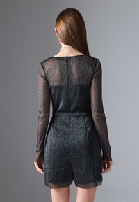 Mono negro brillante con mangas largas transparentes, cuerpo texturizado y pantalones cortos. Presenta un ligero brillo y una cremallera en la parte posterior.