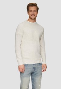 Pull en tricot blanc avec un col rond et des poignets côtelés, porté sur un jean léger en denim déchiré de couleur bleue, présentant une coupe décontractée et une texture douce.