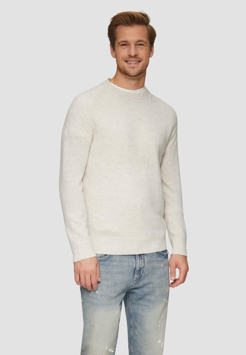 Pull en tricot blanc avec un col rond et des poignets côtelés, porté sur un jean léger en denim déchiré de couleur bleue, présentant une coupe décontractée et une texture douce.