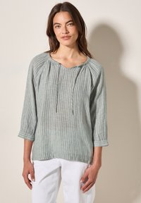 Blusa a righe verde chiaro con scollatura a V, dettagli arricciati sulle spalle e maniche a tre quarti, realizzata in un tessuto strutturato.