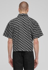 Camisa de manga corta con cuello y un patrón de cuadros en negro y gris. Confeccionada en tejido texturizado, presenta un diseño recortado y un corte relajado.