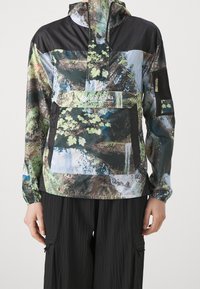 Giacca leggera e colorata con cappuccio, stampa ispirata alla natura che presenta tonalità di verde, marrone e nero; include una tasca frontale e polsini elastici.