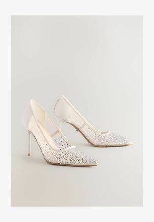 Scarpe bianche con tacco alto e punta affusolata, dotate di una tomaia in rete trasparente decorata con strass argentati nella zona della punta e del tacco.