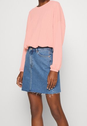 Haut long en rose clair texturé associé à une jupe en denim bleu moyen, avec un ourlet effiloché et un design classique à cinq poches.