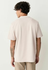 Kurzärmliges Hemd in hellbeige mit Fischgrätmuster, ausgestattet mit einem schlichten Kragen und lockerer Passform, kombiniert mit hellbeigen Hosen.